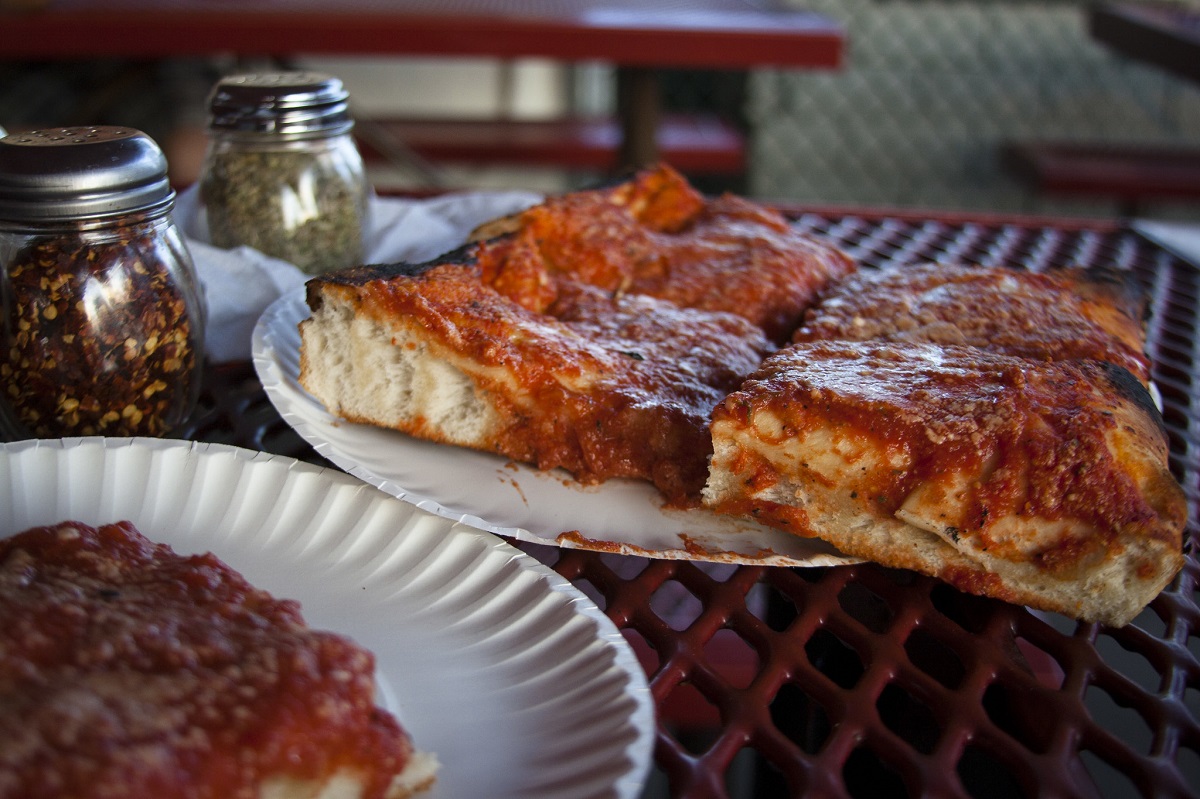 Squares of pizza sit on paper plates that rest on an outdoor picnic table