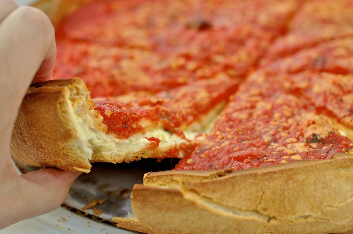 extreme close up of a Chicago deep-dish pizza, with a hand reaching in to take a slice
