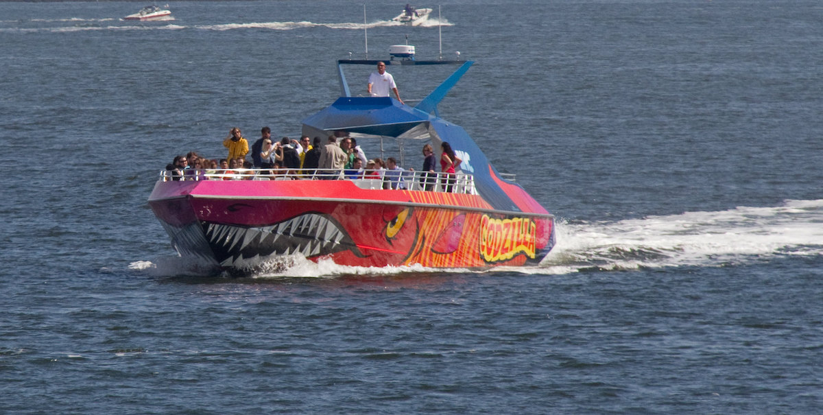 People on a speed boat that is painted bright red and orange in the fashion of an angry fish.