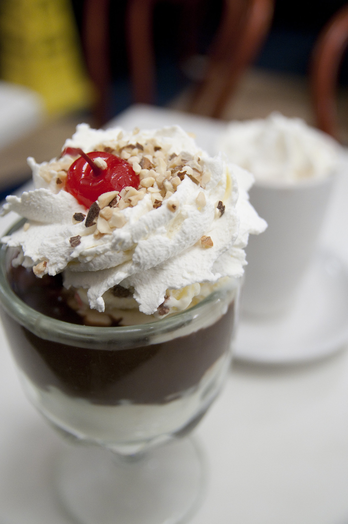Close up of a hot fudge sundae in a clear glass vessel, topped with whipped cream and a cherry.