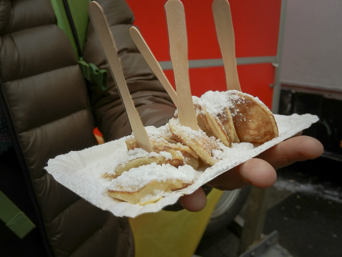 poffertjes covered in snowy sugar on a plate with forks in Amsterdam