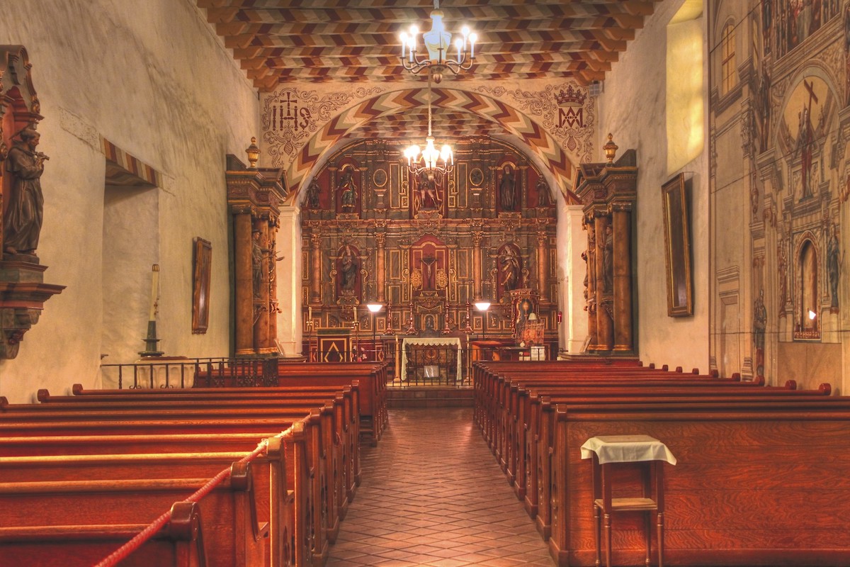 Interior shot of the chapel at Mission Dolores. Wooden pews line up facing the ornately decorated pulpit