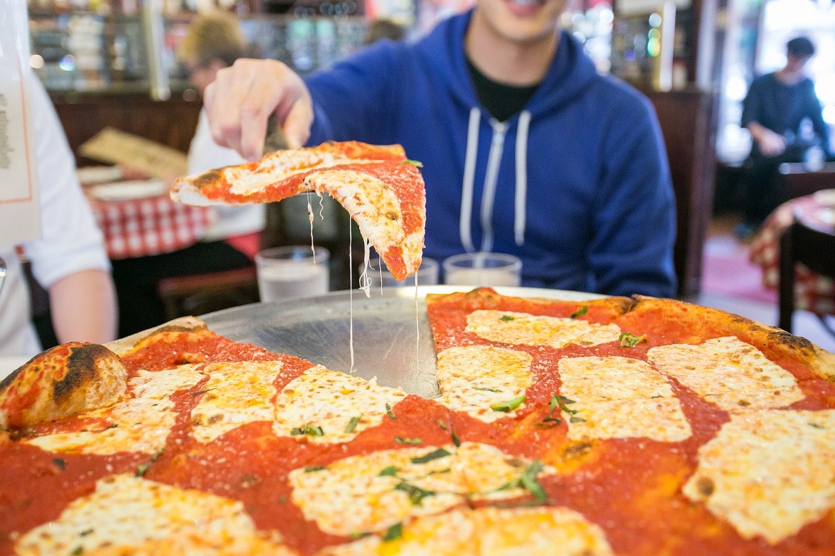 A man serves up one slice of pizza from an enormous pie