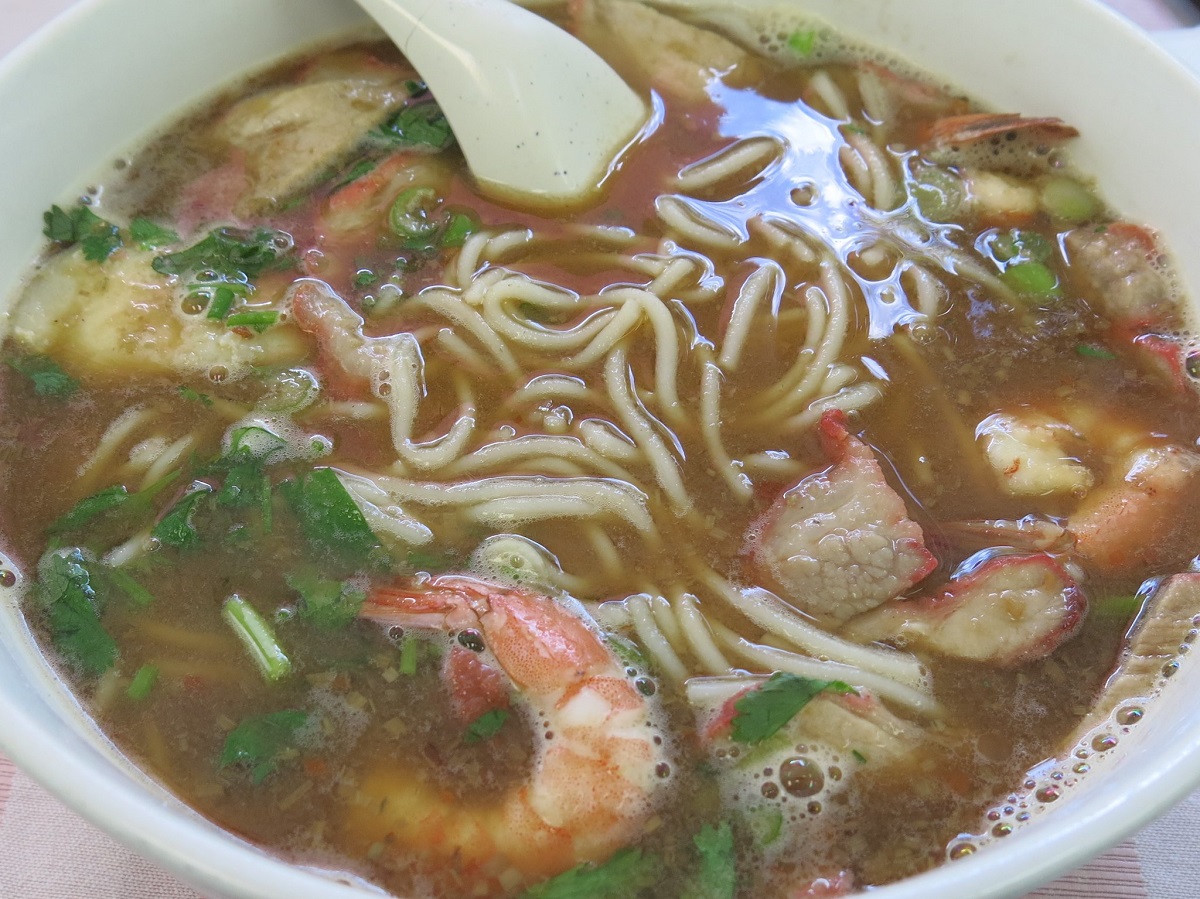 A bowl of pho with noodles, shrimp, cilantro, beef, and a spoon in a San Francisco cafe