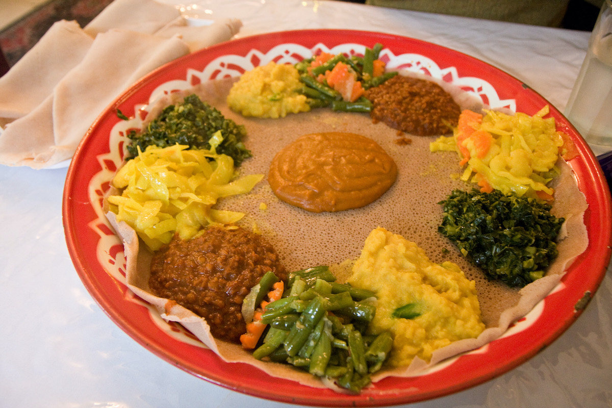 Sharing platter of vegetarian Ethiopian food with vegetables and sauces over spongy bread