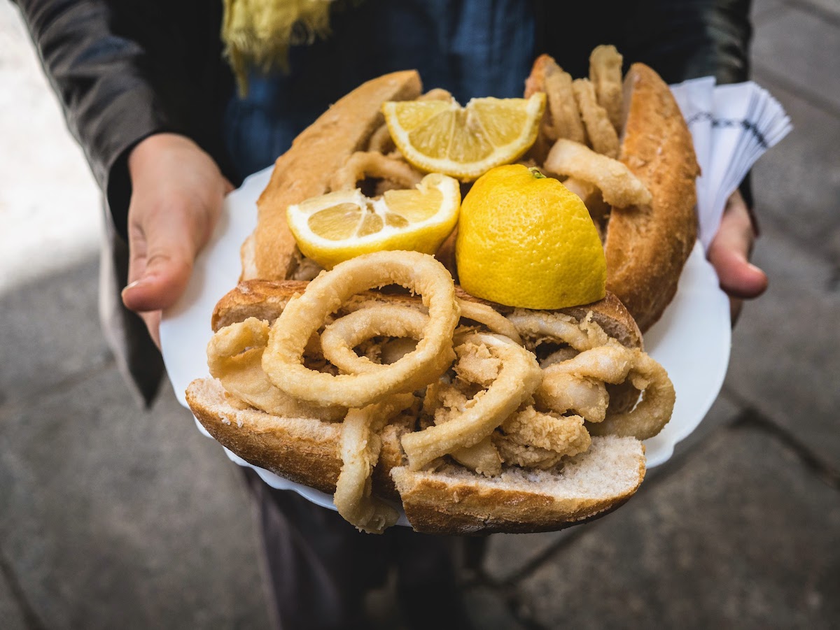Tray of fried calamari sandwiches on baguette rolls with lemon wedges.