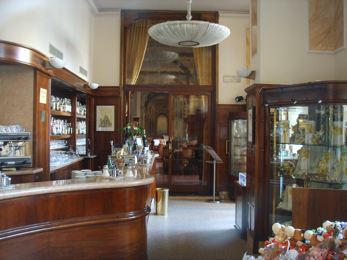 Interior of a historical cafe in Florence, Italy with a wraparound bar, dark wood details and a 1920s light fixture