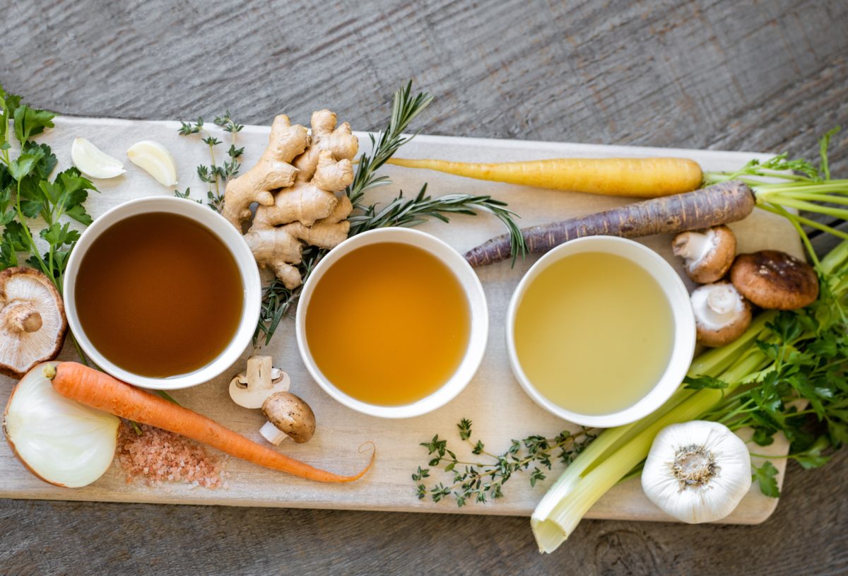 Three small bowls of broth surrounded by vegetables