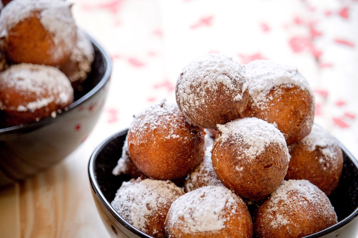 fried dough balls with powdered sugar in black bowl