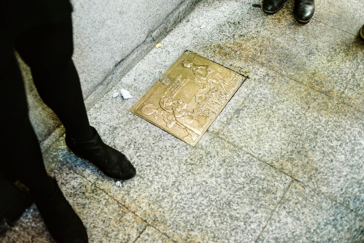 Overhead shot of a plaque set into the sidewalk outside a building.