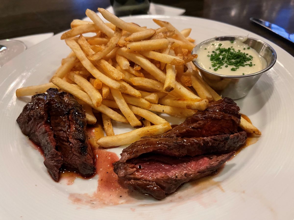 close-up of steak and fries with a side of sauce. 