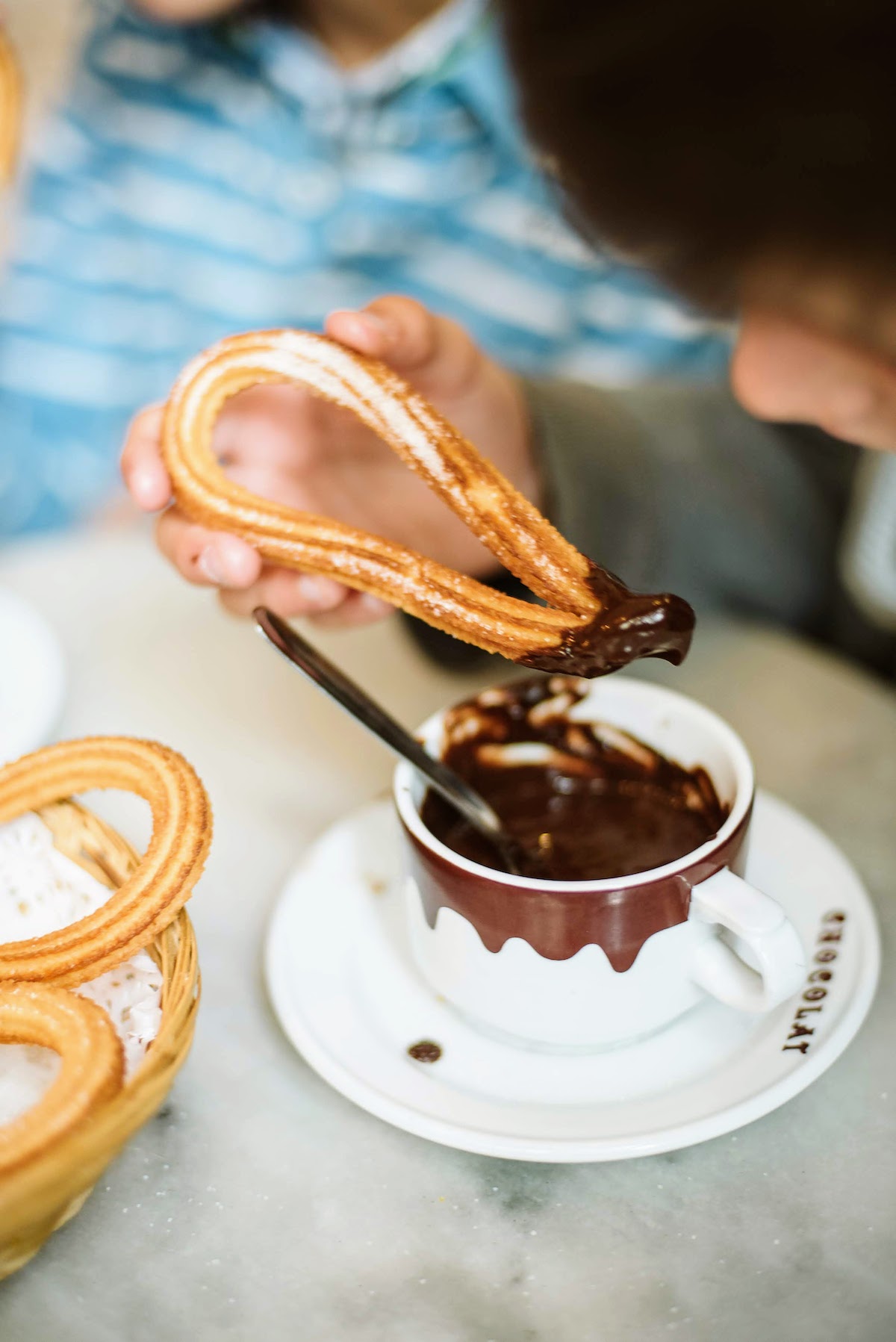 Child's hand dipping sugar-covered churros into a mug of thick hot chocolate