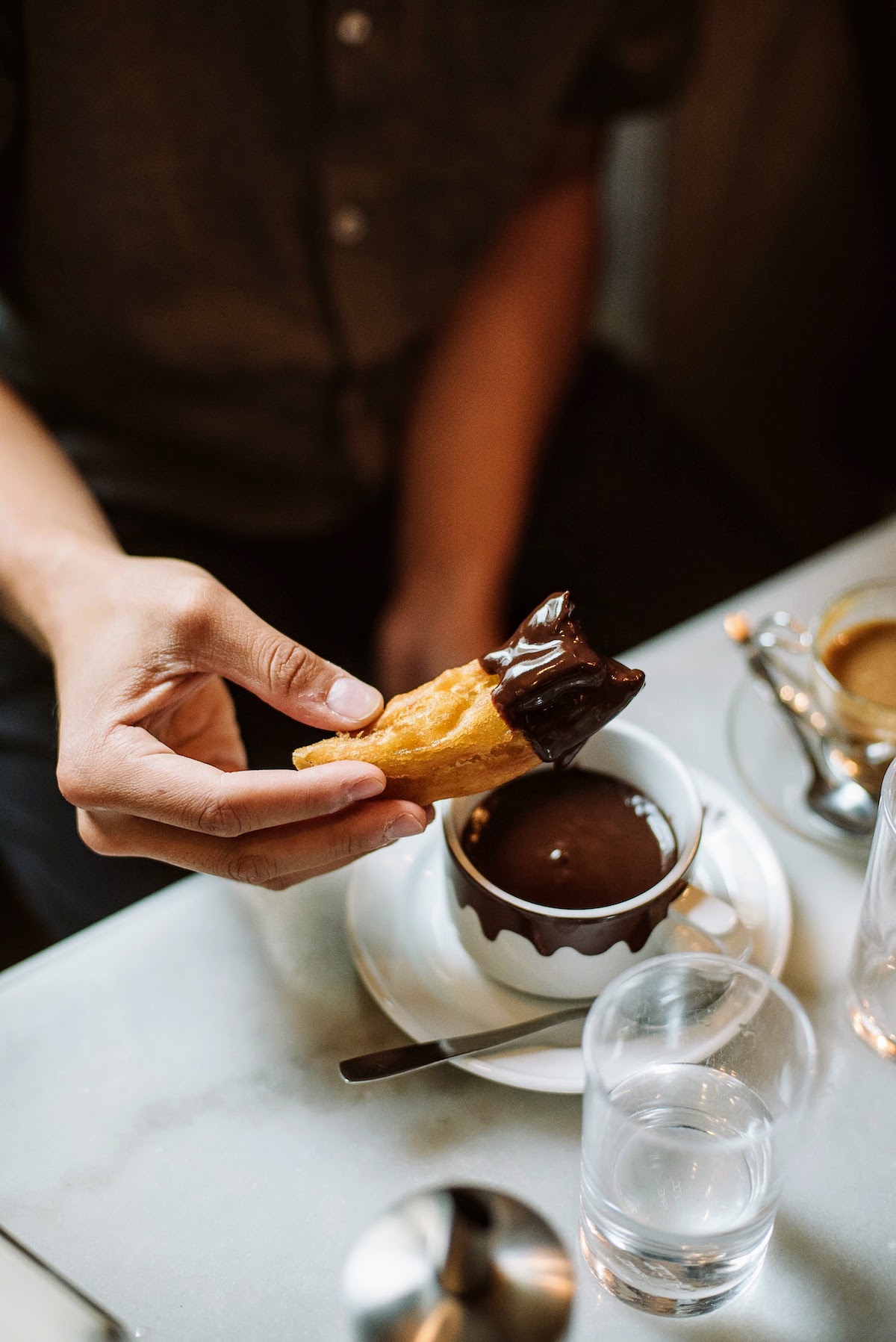 Person dipping thick churros into hot chocolate