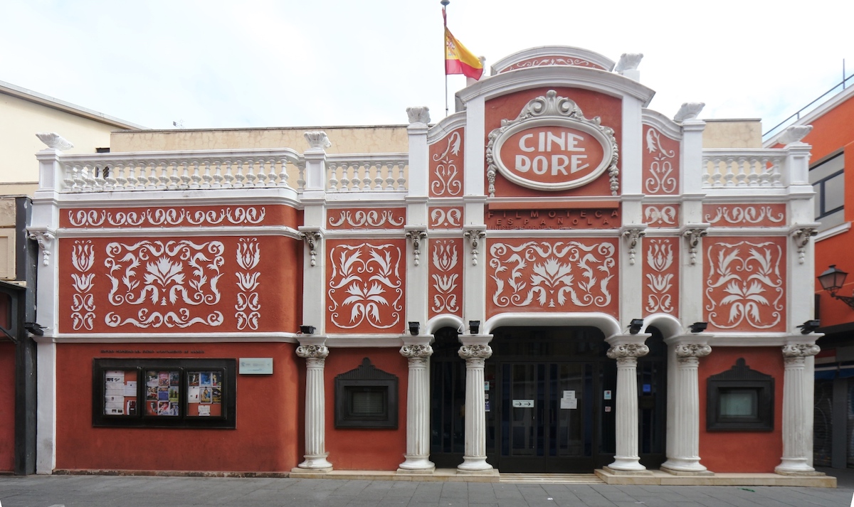 Exterior of a historic movie theater with red stone and white details and columns.