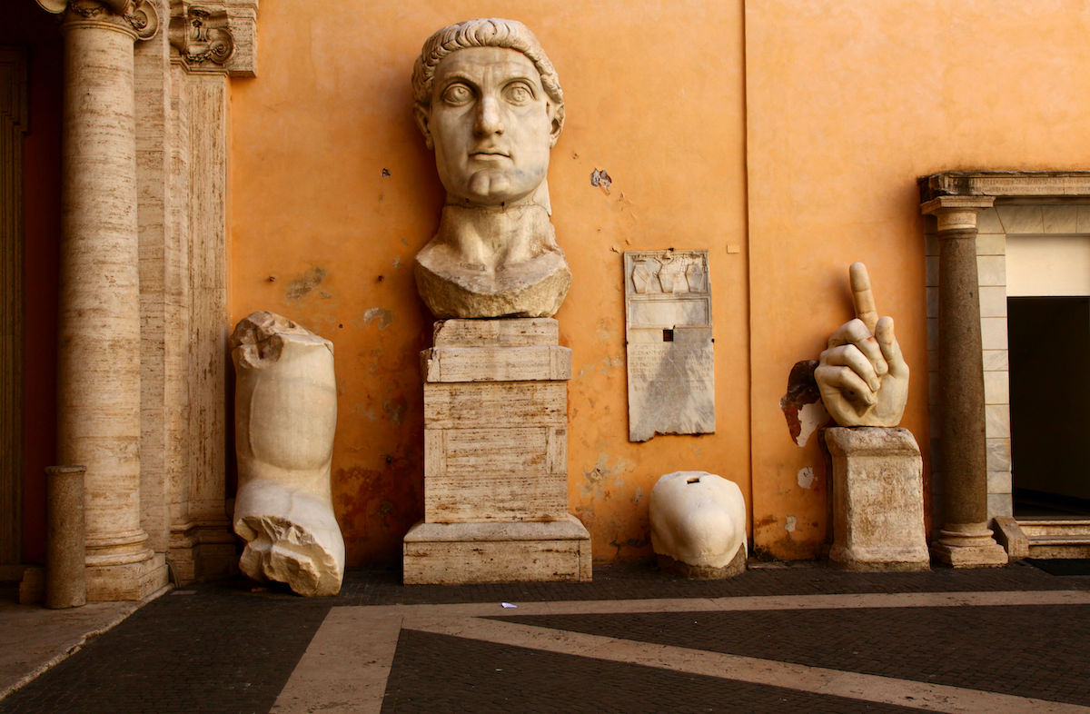 Ancient Roman marble columns, the head of a statue of the emperor Constantine, and other fragments displayed against an orange wall.