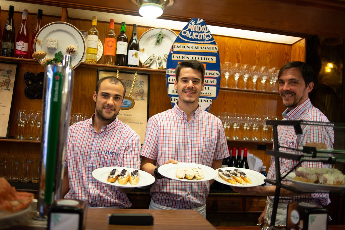 Three smiling servers at a Basque bar holding plates of pintxos at Bar Txapetxa.