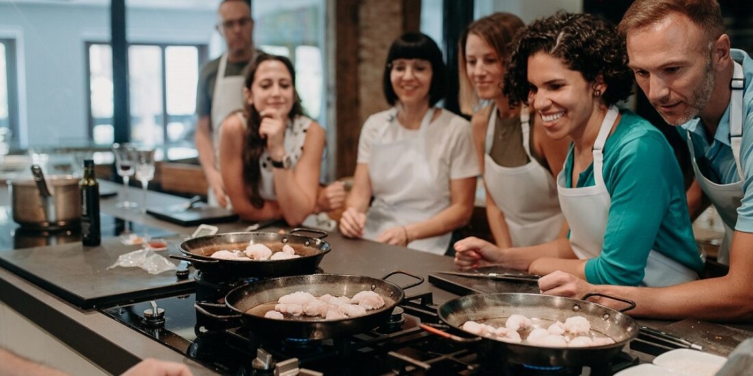 Students in a Devour cooking class look on at their paellas on the stove