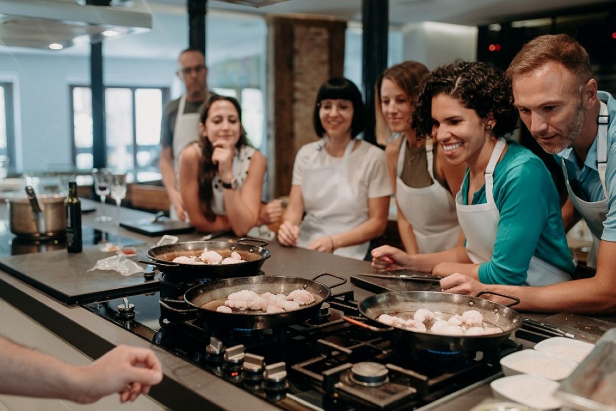 Students in a Devour cooking class look on at their paellas on the stove