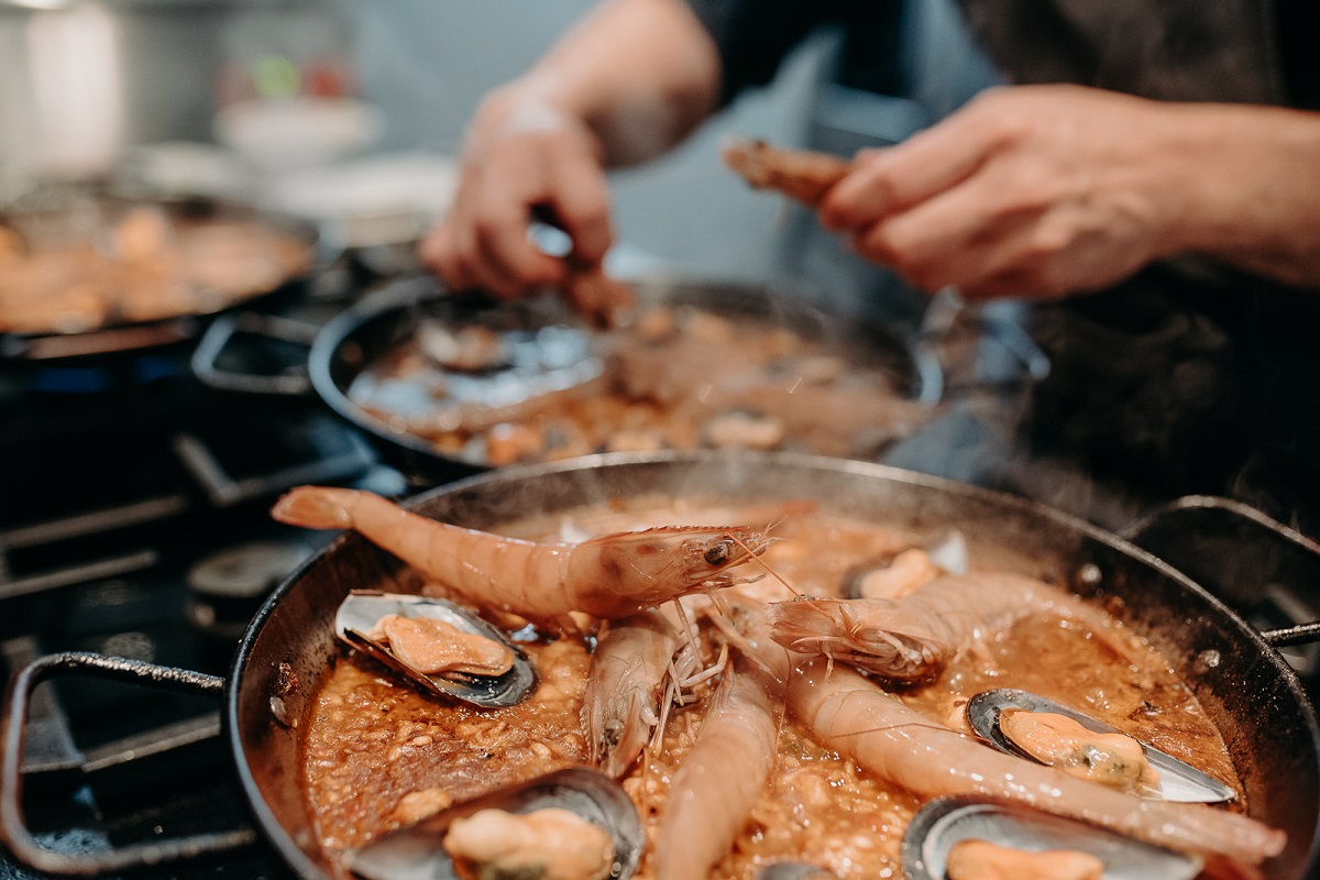 Stovetop with paella pans and paella cooking with shrimp and chef's hands in the background of the kitchen