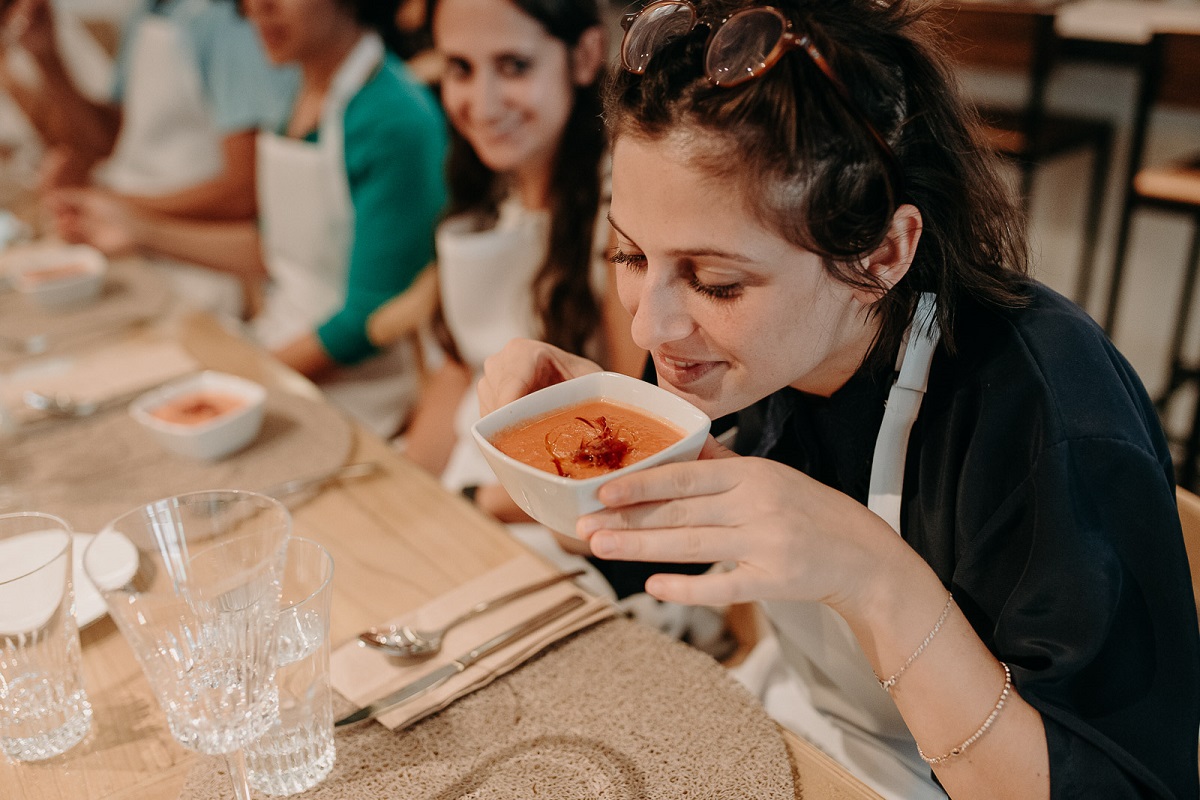 Woman at cooking class leaning down to smell her homemade gazpacho during a Spanish cooking class