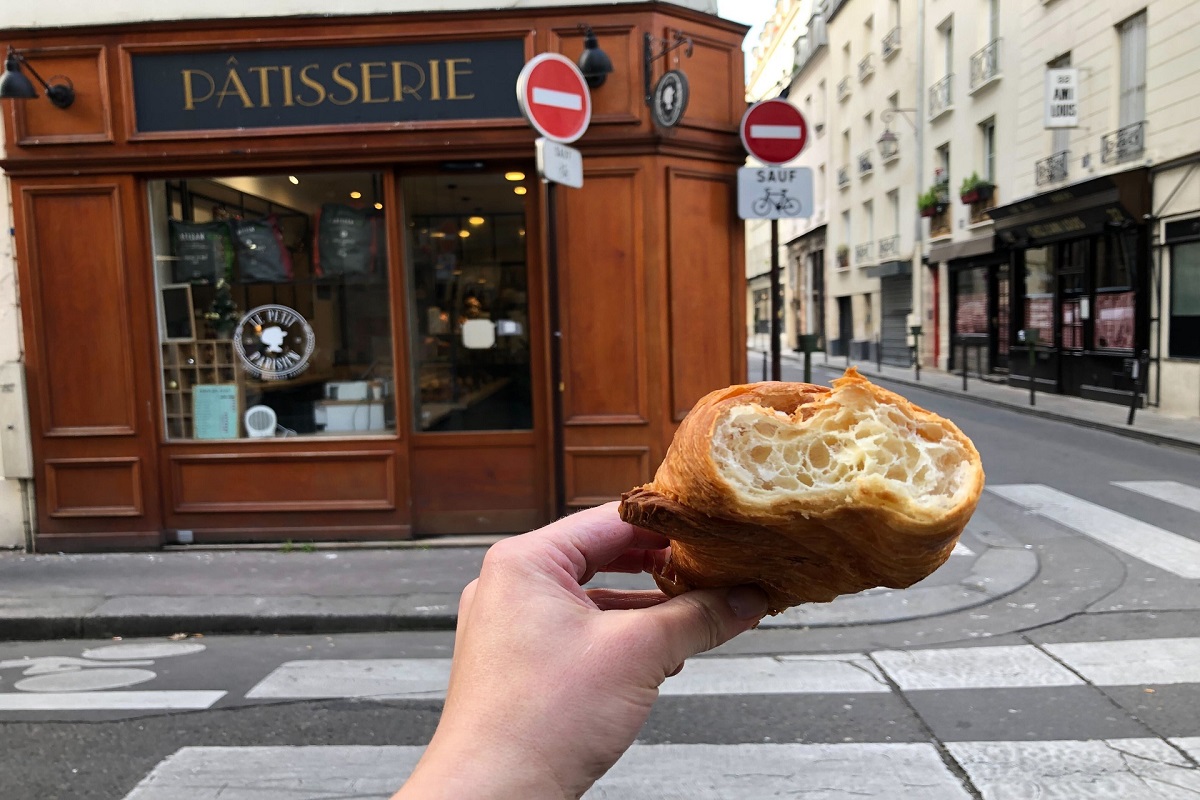 Hand holding croissant up with bite on street in front of a bakery in Paris