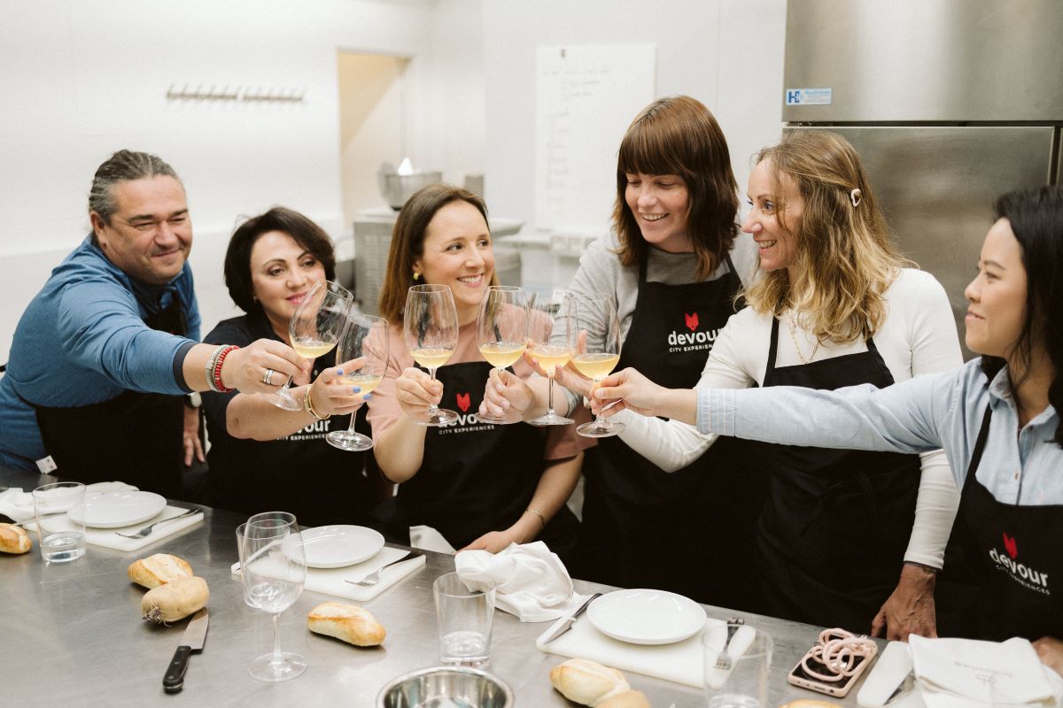 A group of people in a cooking class take a moment to cheers with their wine glasses before the class starts