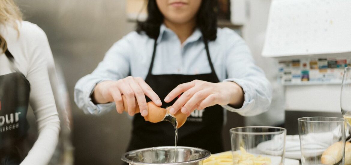 A girl cracks an egg over a bowl while preparing a recipe