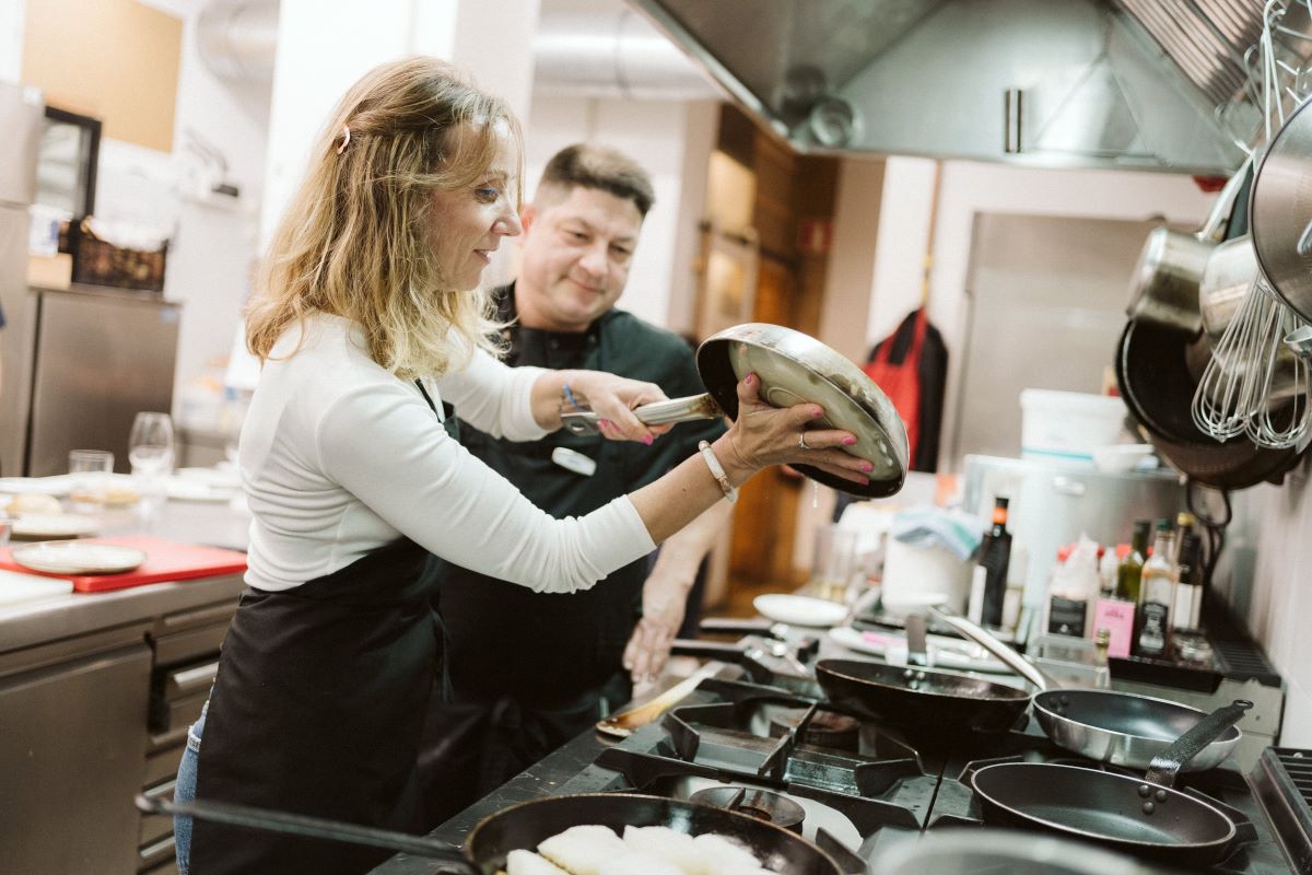 A chef helps a student with a task in the kitchen during a cooking class