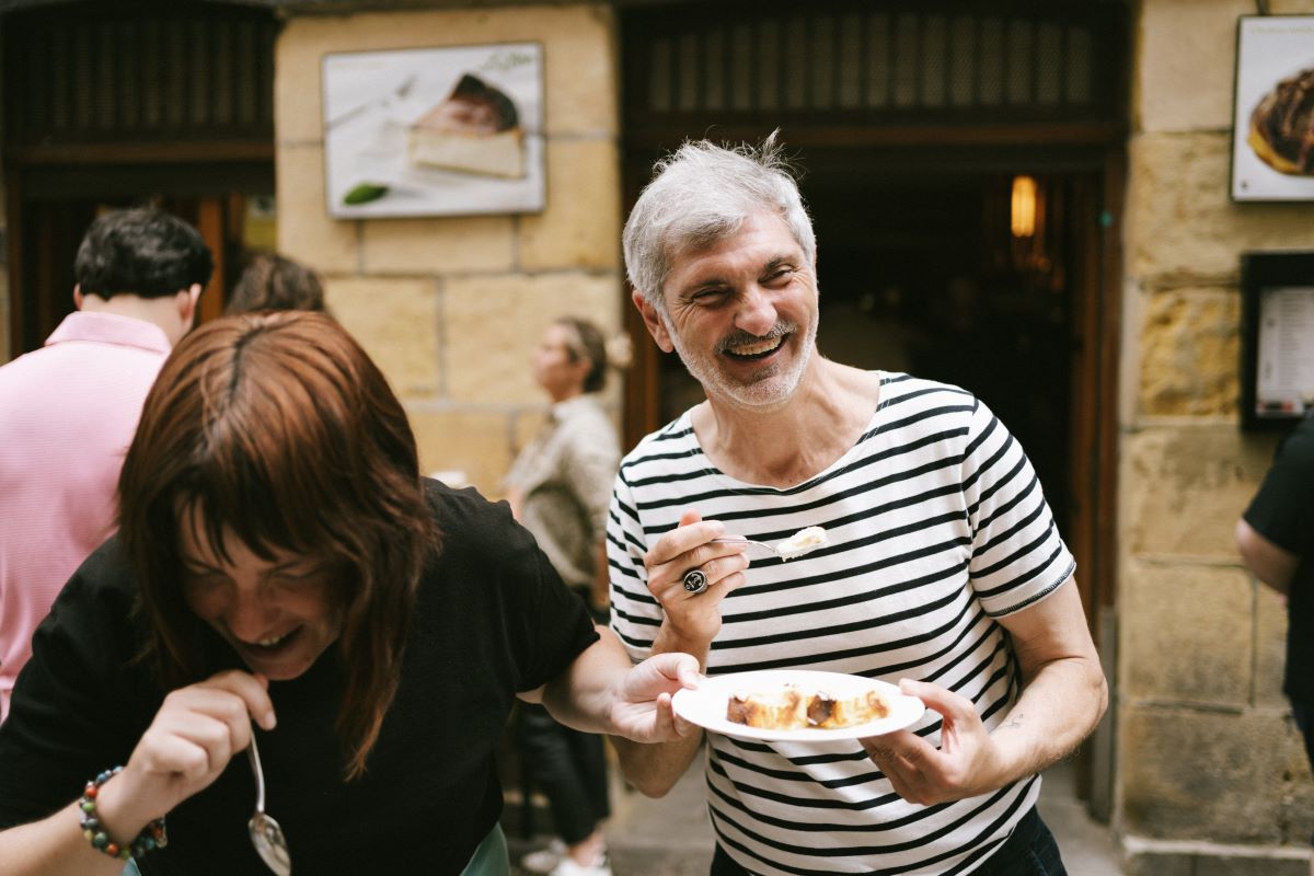 A pair of guests having a laugh while eating cheesecake on the streets of San Sebastian