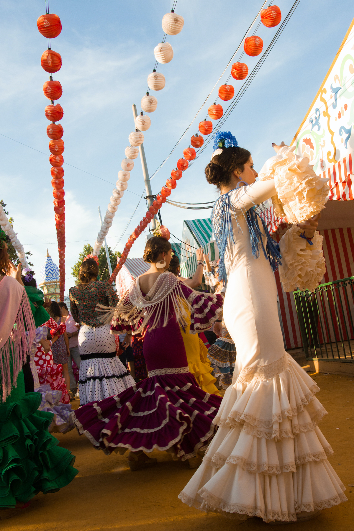 Group of women in flamenco dresses beneath three strings of paper lanterns.