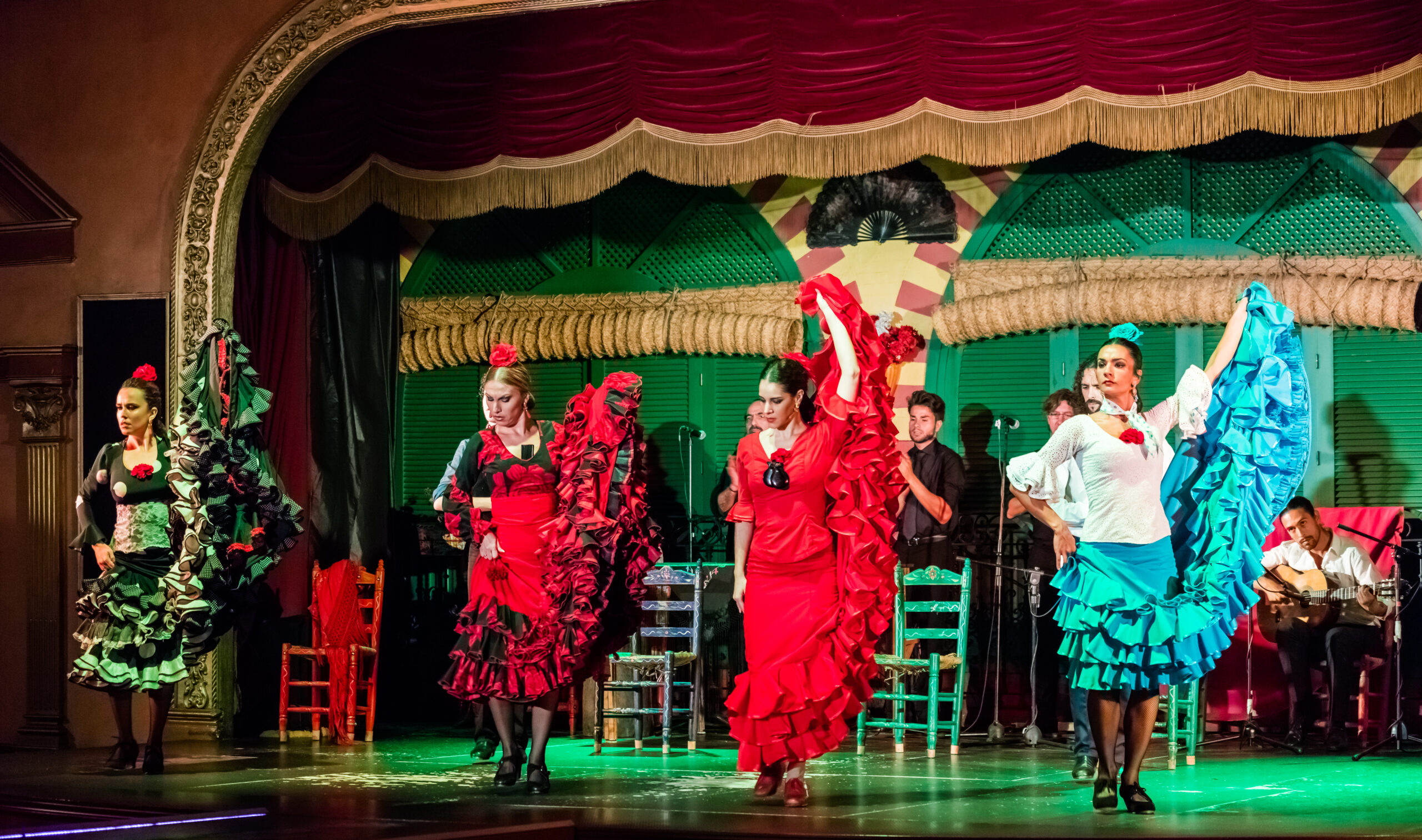 Four flamenco dancers in sevillana dresses perfoming on a stage 