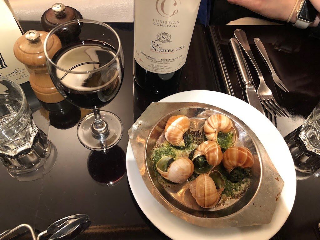 Plate of snails or escargot in butter and herbs with wine at a table in Paris