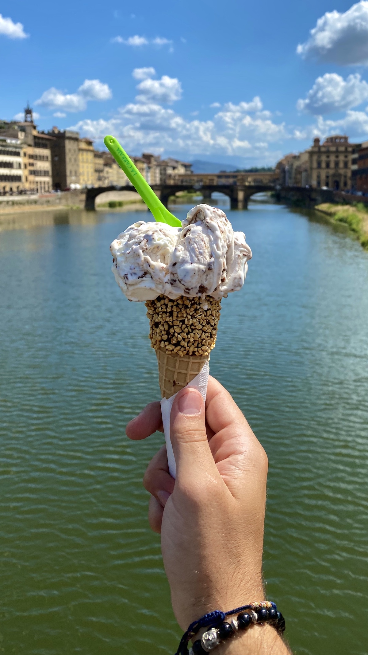 Gelato cone being held up in front of a bridge over the river in Florence, Italy