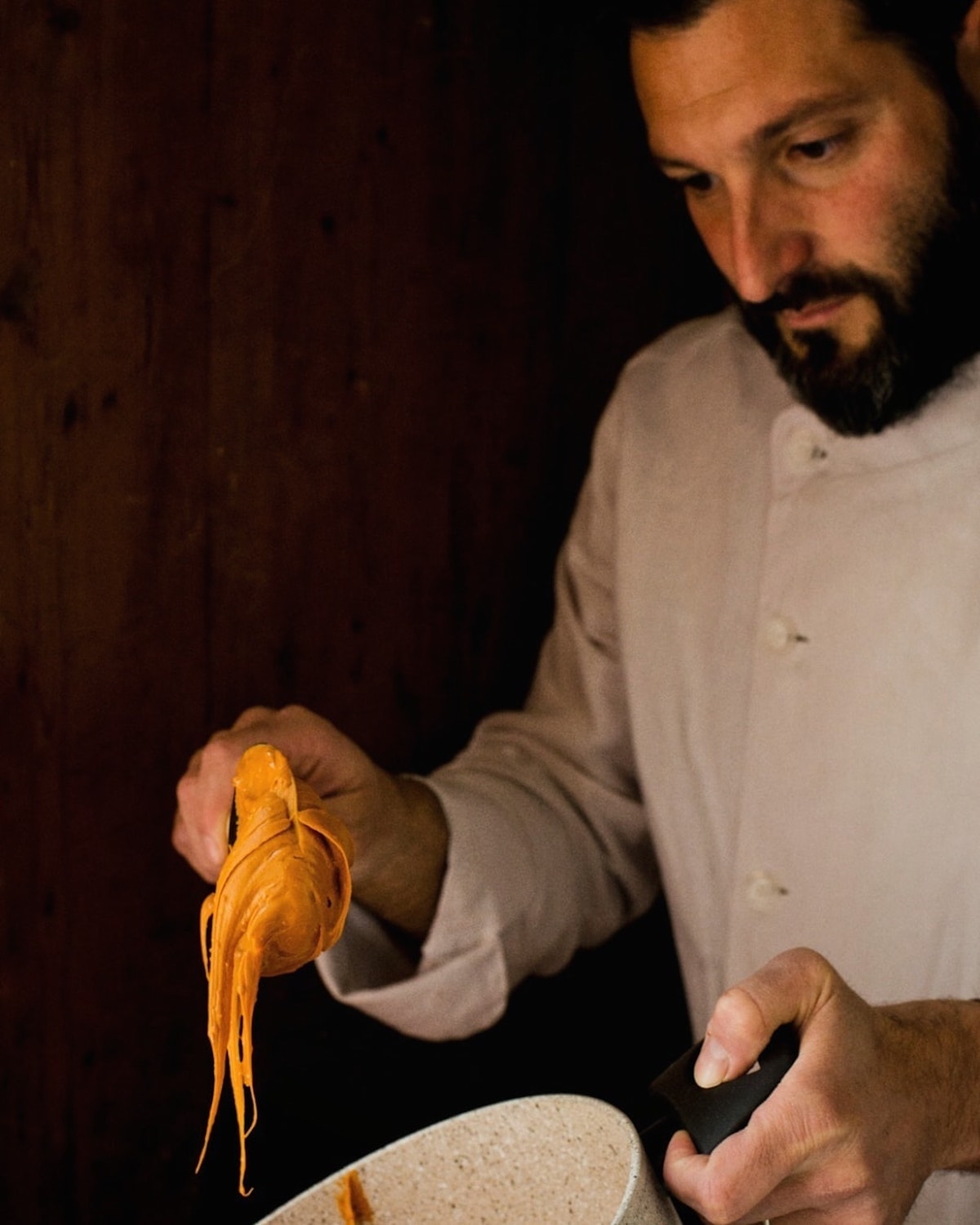 A man in a white chef's coat scooping brown ice cream