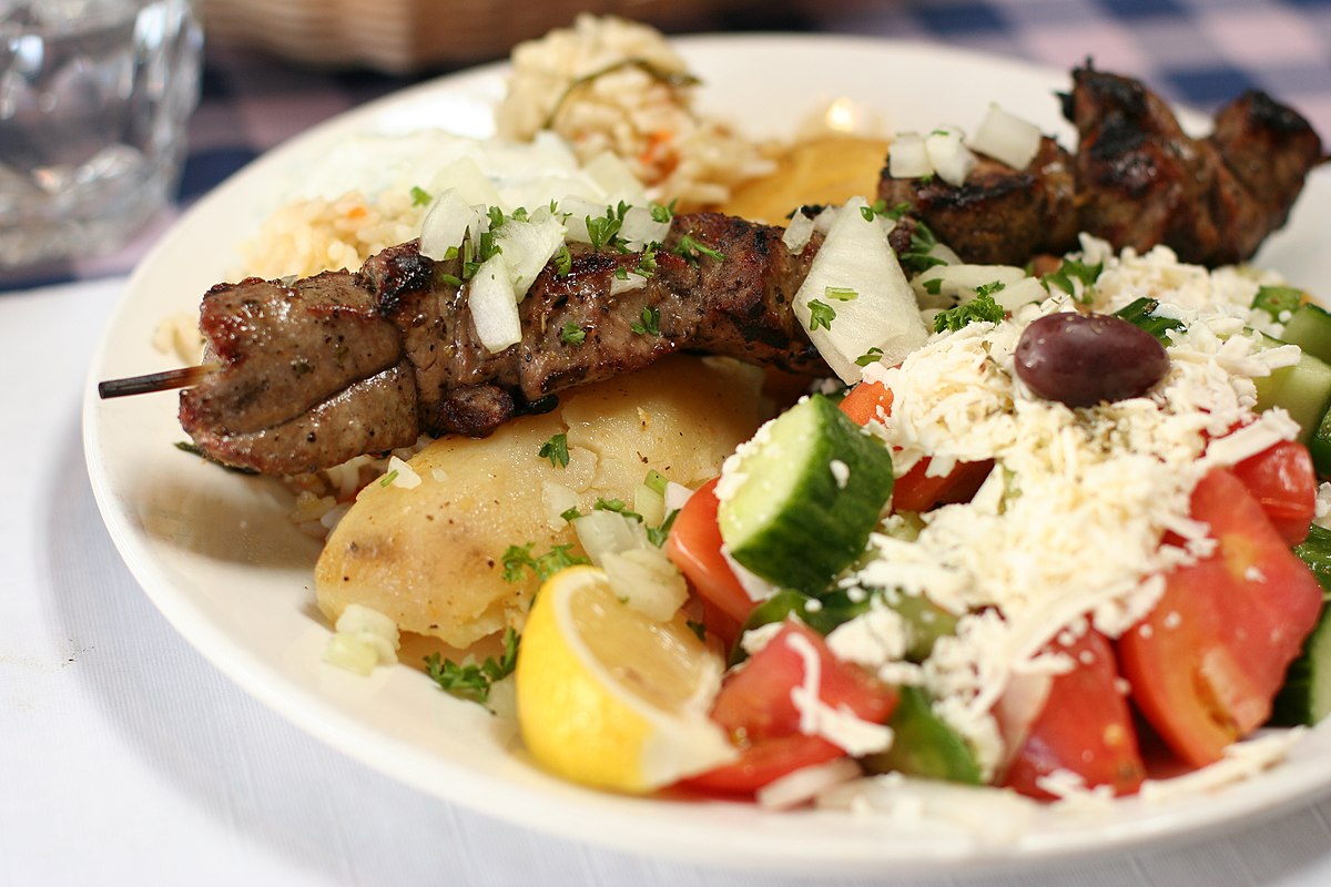 a plate of traditional greek food including lamb and salad with veggies and cheese