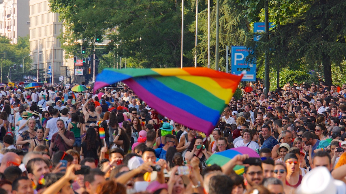 Rainbow LGBTQ+ flag waving above a large crowd at a Pride celebration.