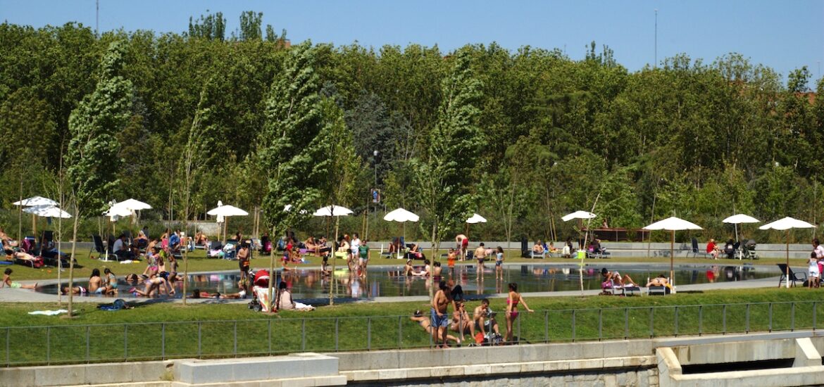 Riverside beach area full of people in bathing suits relaxing under umbrellas.