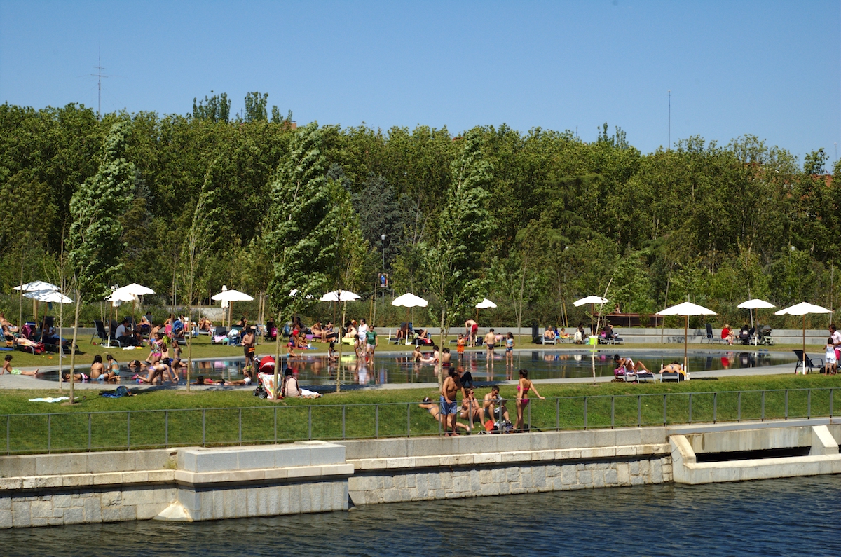 Riverside beach area full of people in bathing suits relaxing under umbrellas.