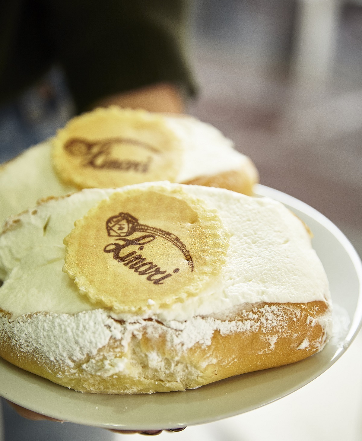 Close up of bread stuffed with cream and a cookie that says "Linari" on a white plate.