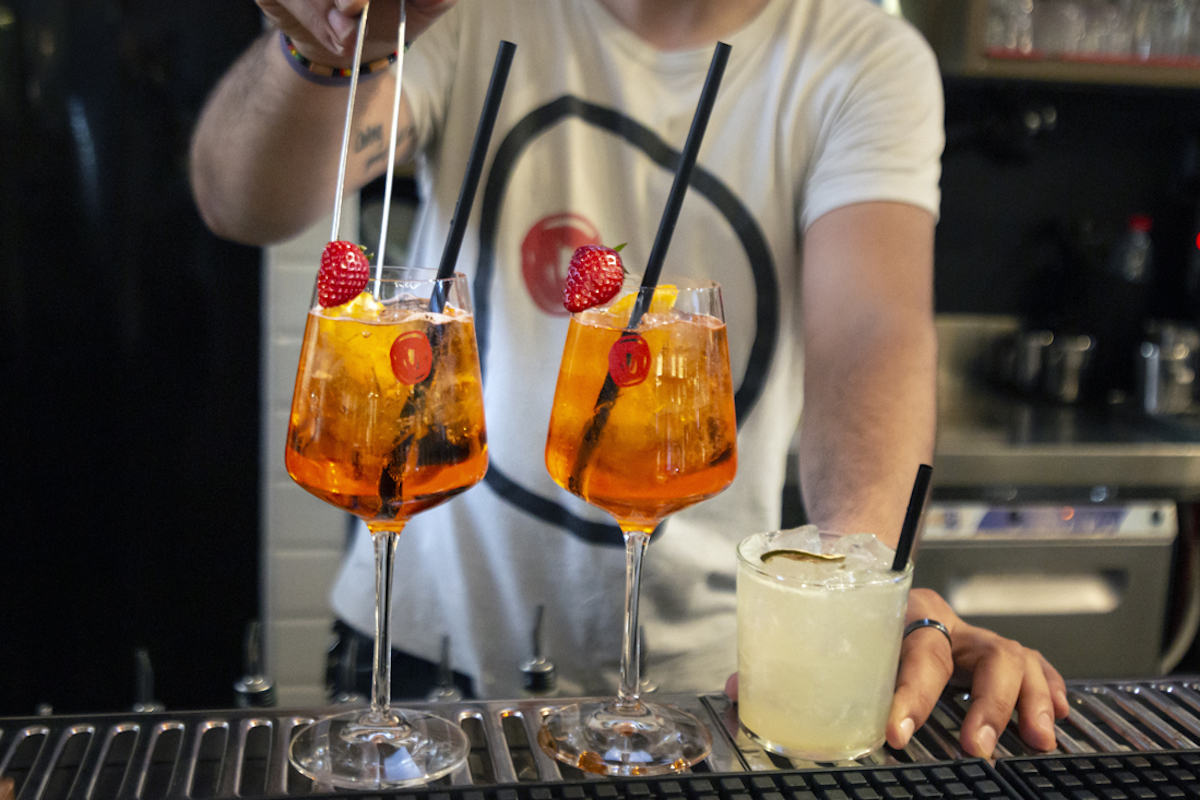 A bartender making bright orange cocktails in tall stem glasses