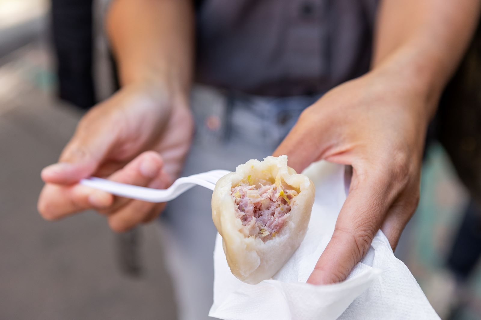 Person using a plastic fork to bite into a Chinese dumpling in New York City, one of the best ways to see the Lower East Side