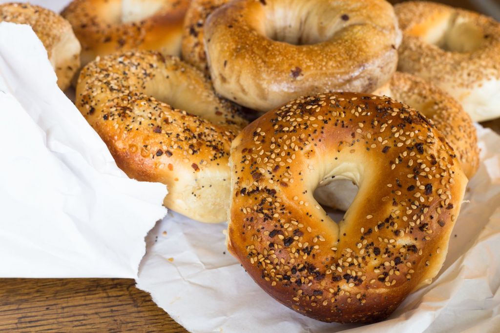 several bagels on a white paper bag with poppy and sesame seeds on top, one of the best ways to see the Lower East Side