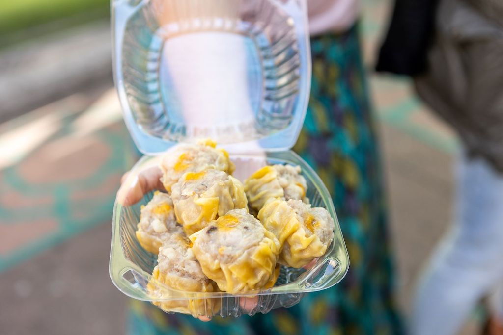 Person on street holding a plastic container of chinese dumplings