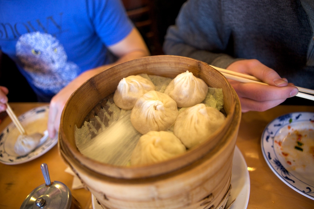 Five Chinese soup dumplings in a round wooden serving basket.
