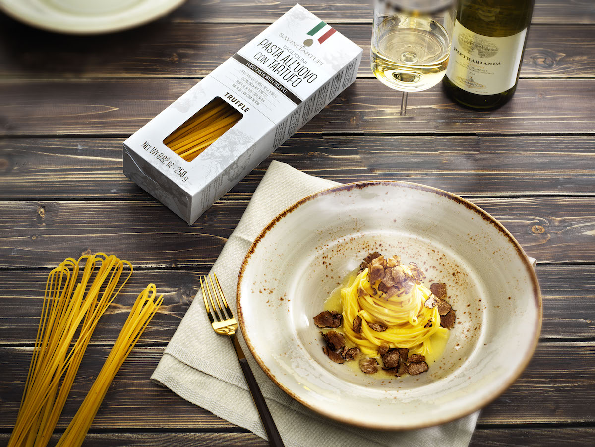 Plate of truffle pasta on a wooden tabletop with a white box of the same spaghetti noodles and a few loose dry noodles to the left