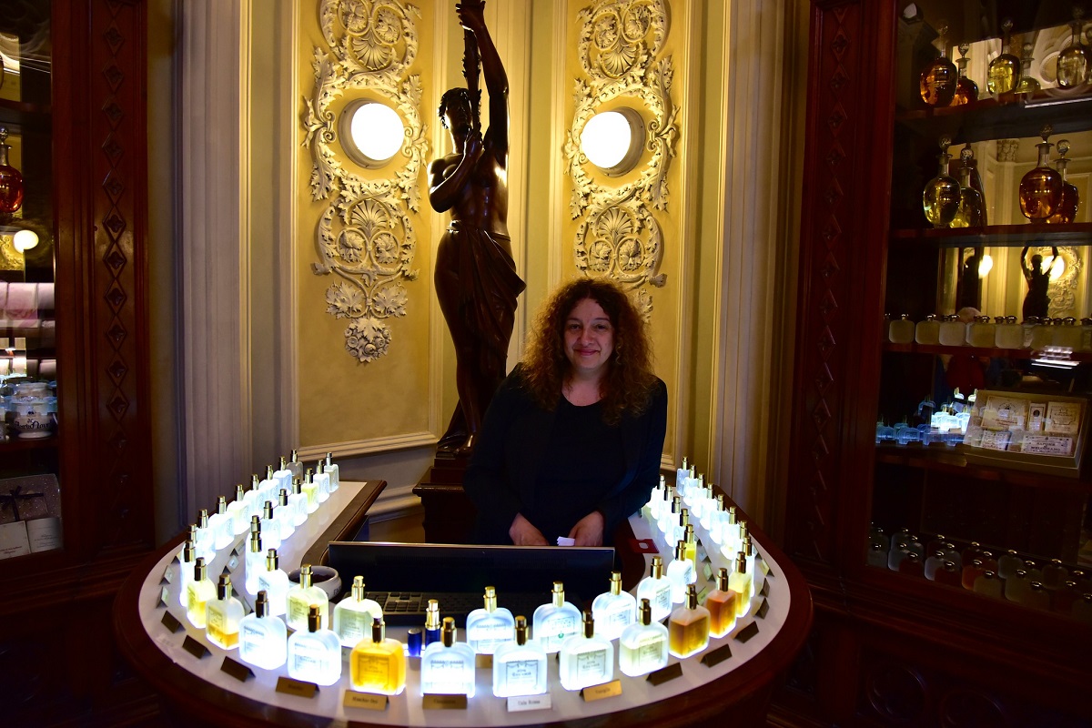A woman stands at a counter surrounded by multicolored perfume bottles.