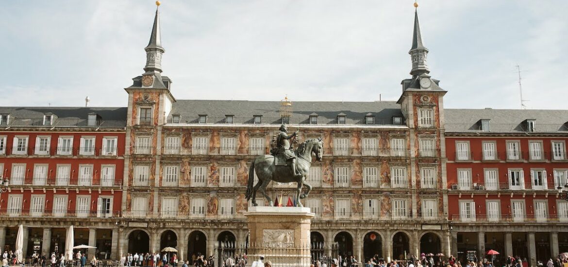 View of the central building of Madrid's Plaza Mayor with a statue of a man on horseback in the foreground.