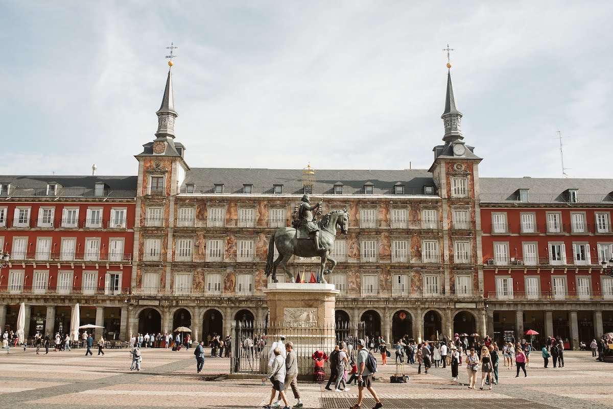 View of the central building of Madrid's Plaza Mayor with a statue of a man on horseback in the foreground.