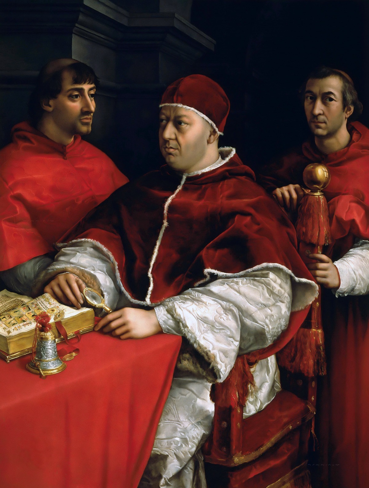 A Catholic pope and two cardinals in red robes gather around a table with a book and a red tablecloth