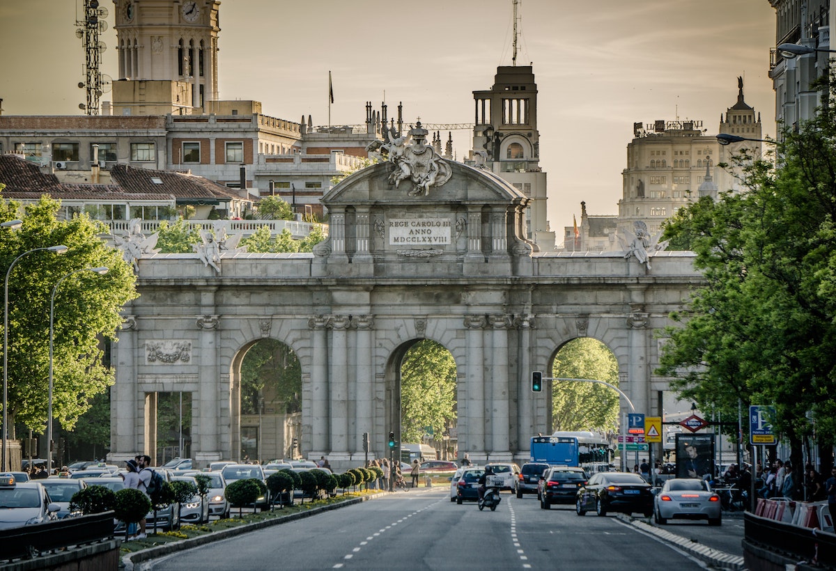 Traffic in front of the Puerta de Alcalá arched gateway monument in central Madrid with the city skyline in the background.